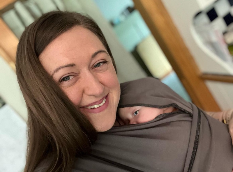 Caitlin Raftis with her infant son wrapped in a fabric carrier on her chest, his eyes peeking out. She offers counseling services in Farminton, Connecticut.